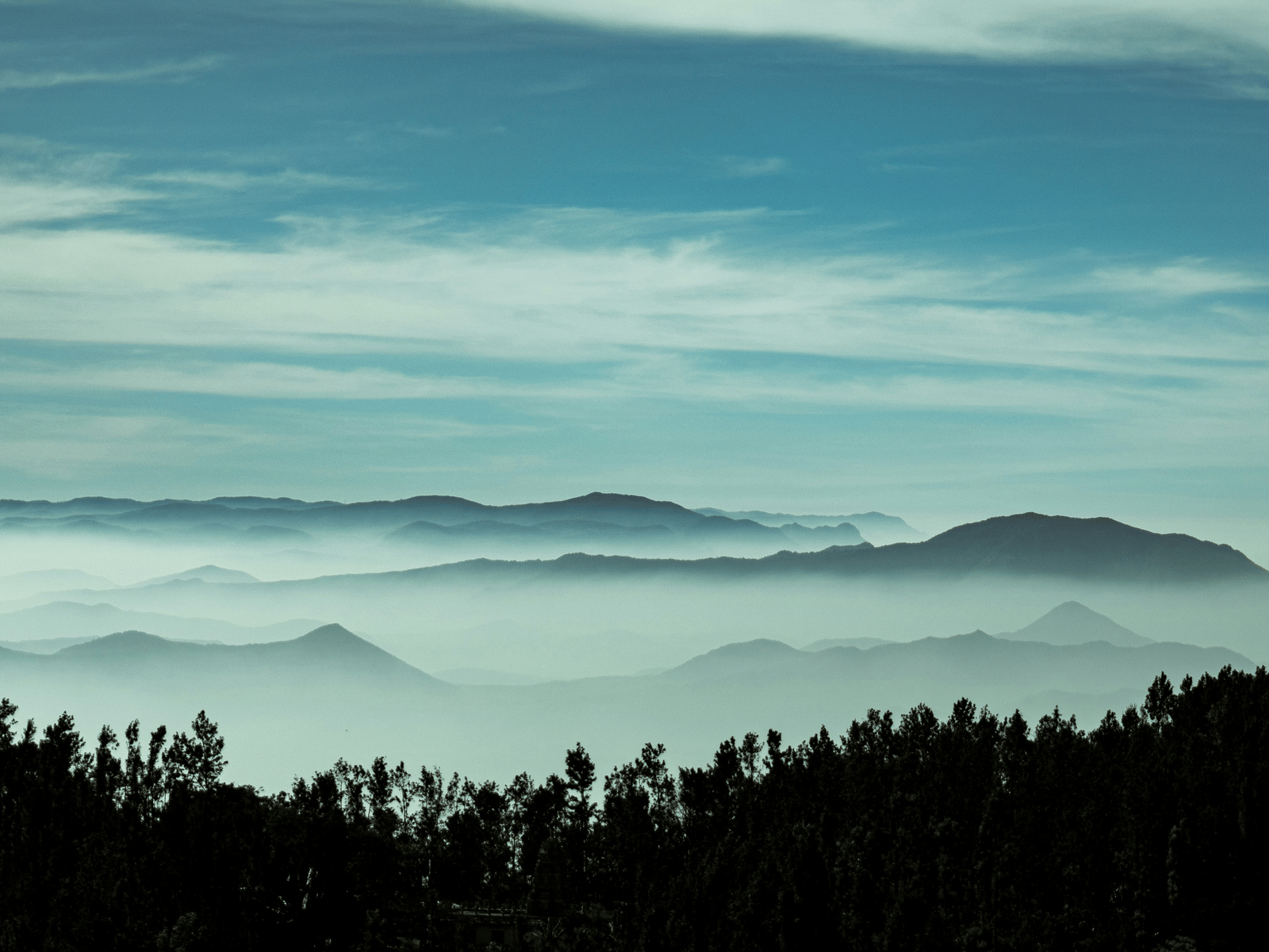 Sunrise over a forested hill range with layers of hills fading into the horizon.