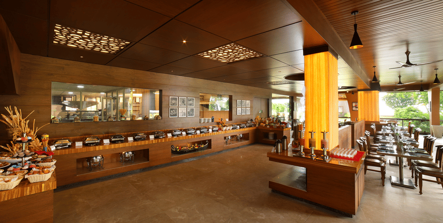 Aambal Restaurant at Uday Backwater Resort, with tables set on one side overlooking the outdoors and buffet counters on the other