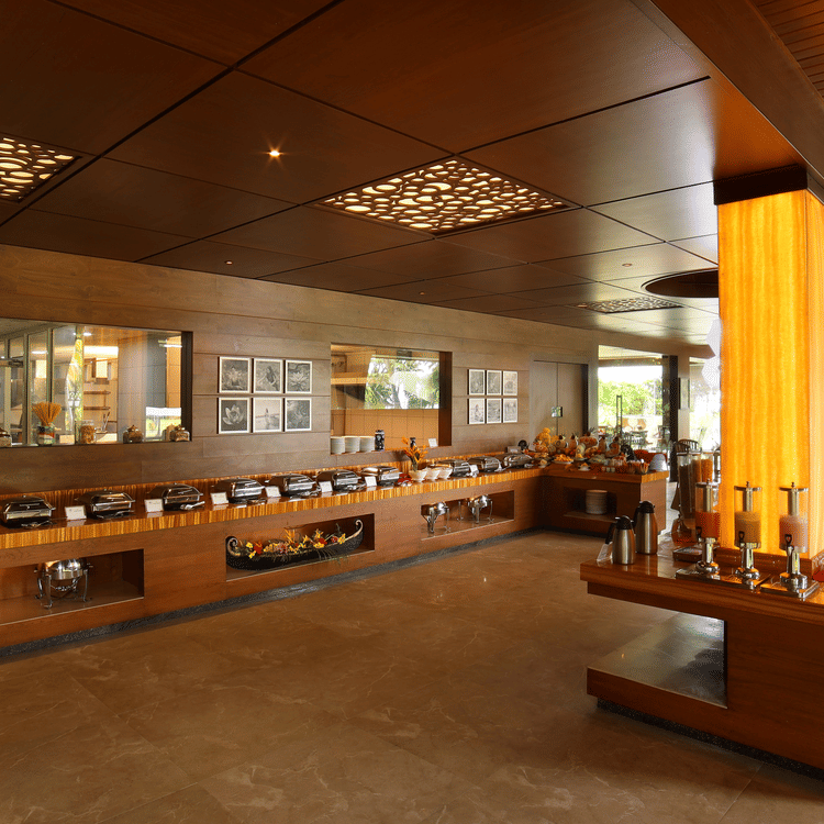 Aambal Restaurant at Uday Backwater Resort, with tables set on one side overlooking the outdoors and buffet counters on the other