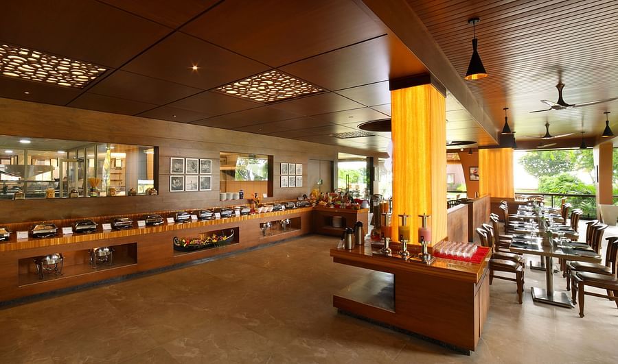 Aambal Restaurant at Uday Backwater Resort, with tables set on one side overlooking the outdoors and buffet counters on the other