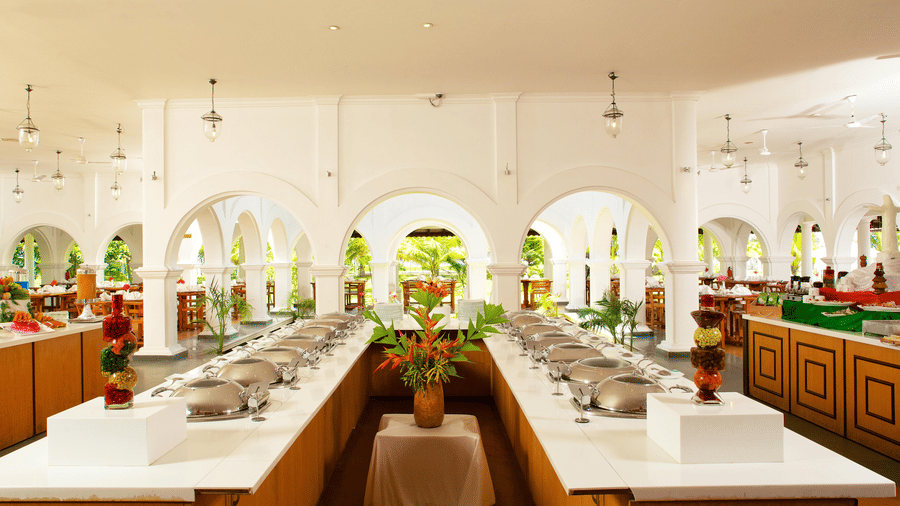 An indoor restaurant buffet area featuring a U-shaped counter with food warmers set against white arched walls | Le Pondy