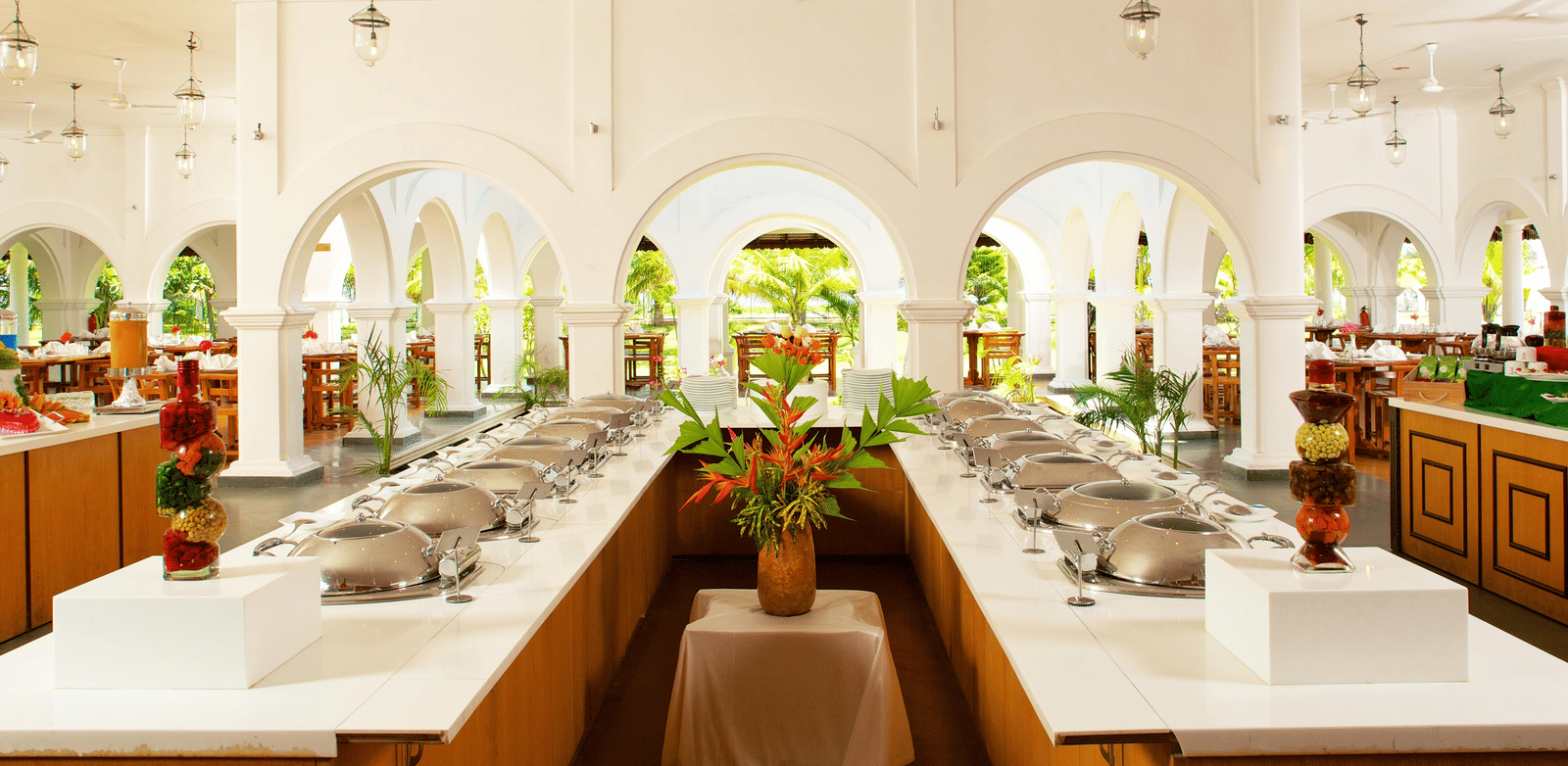 An indoor restaurant buffet area featuring a U-shaped counter with food warmers set against white arched walls | Le Pondy