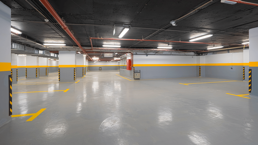 Parking space of Grand Iva Hotel, Abha, situated in the basement with ample overhead lighting, painted pillars, and flooring reflecting the lights.