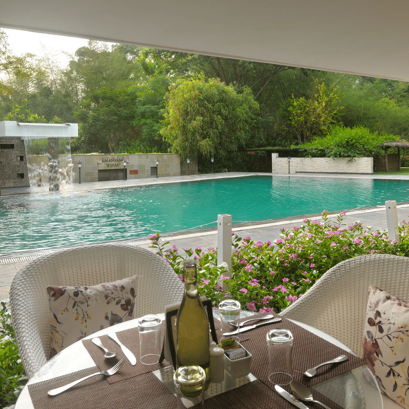 Outdoor poolside dining area with tables set and a pool in the background at Amanvana Spa Resort, Coorg - Luxury Resort
