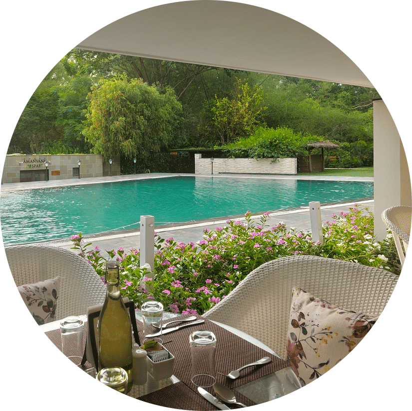 Outdoor poolside dining area with tables set and a pool in the background at Amanvana Spa Resort, Coorg - Luxury Resort