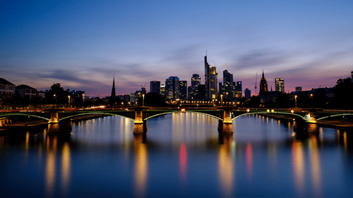 An overview of a bridge over a waterbody as seen during twilight with the lights on.