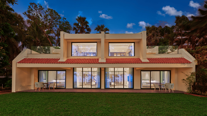 An exterior view of the villa at The Resort, Mumbai, with a manicured garden in front and trees surrounding it.