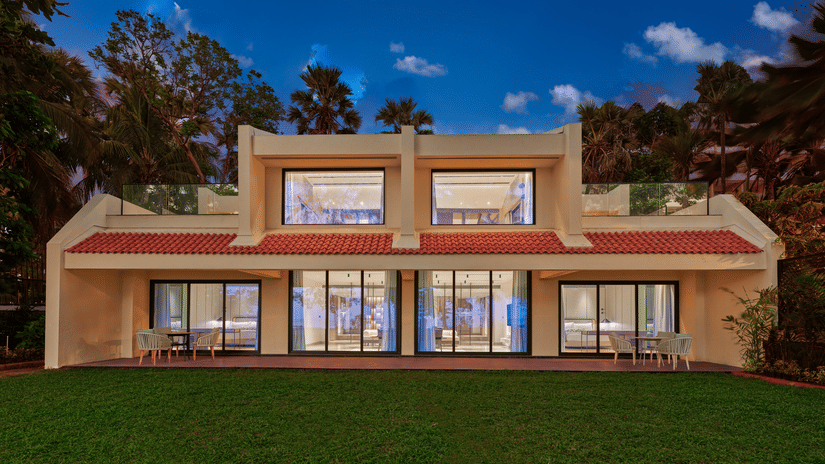 An exterior view of the villa at The Resort, Mumbai, with a manicured garden in front and trees surrounding it.