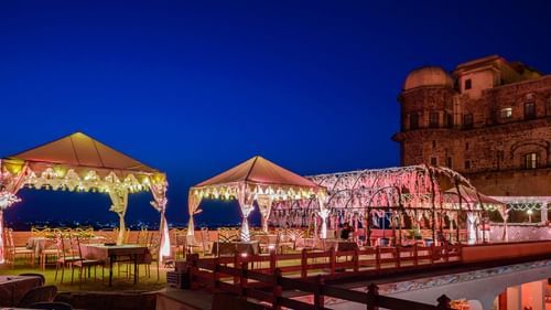 Two tented structures and a larger illuminated structure stand on a terrace next to a building at Tijara Fort-Palace - 19th Century, Alwar.