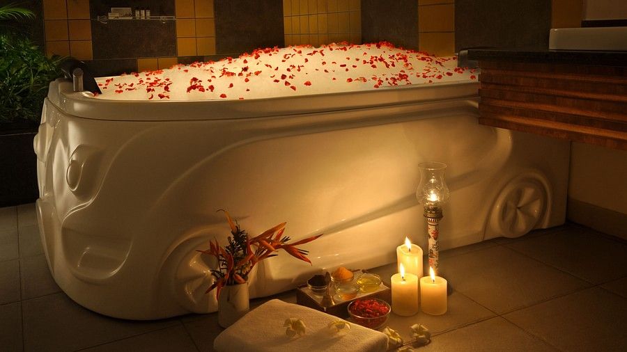 Elegant bathtub with rose petals floating on water, candles, and flowers beside it.
