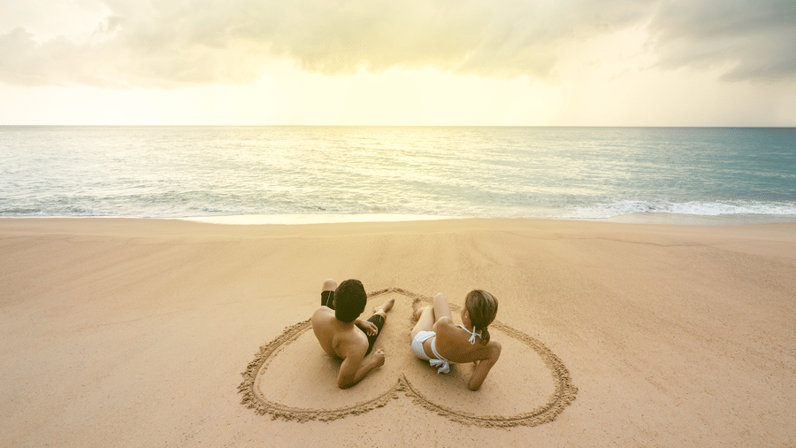 couple sitting in a beach inside a heart shape drawing on the sand during sunset