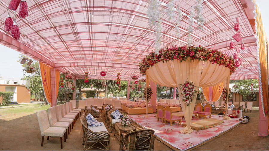 An outdoor event area featuring seating arranged under a pink fabric canopy with a decorated central dome structure at Garh Govind.