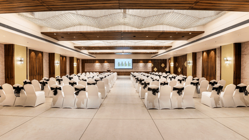 A banquet hall in Candolim set up with round tables, white chairs, and presentation screentowering hotel buildings featuring balconies, a signage with hotel name, and surrounded by lush greenery, set against a cloudy sky - Golden Tulip, Candolim, Goa