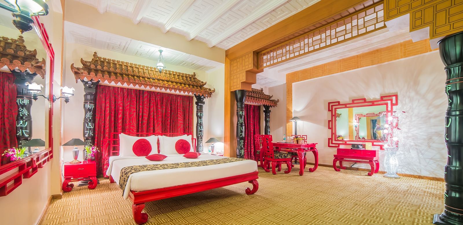 A grand hotel suite with an opulent red and white decor, large bed, and seating area, reflecting a traditional style at Sitara Luxury Hotel in Hyderabad near Ramoji Film City.