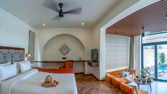 A bedroom with a large bed, an arched entryway leading to a sitting area with a sofa, and sliding glass doors opening to an outdoor area at The Golden Tusk, Jim Corbett