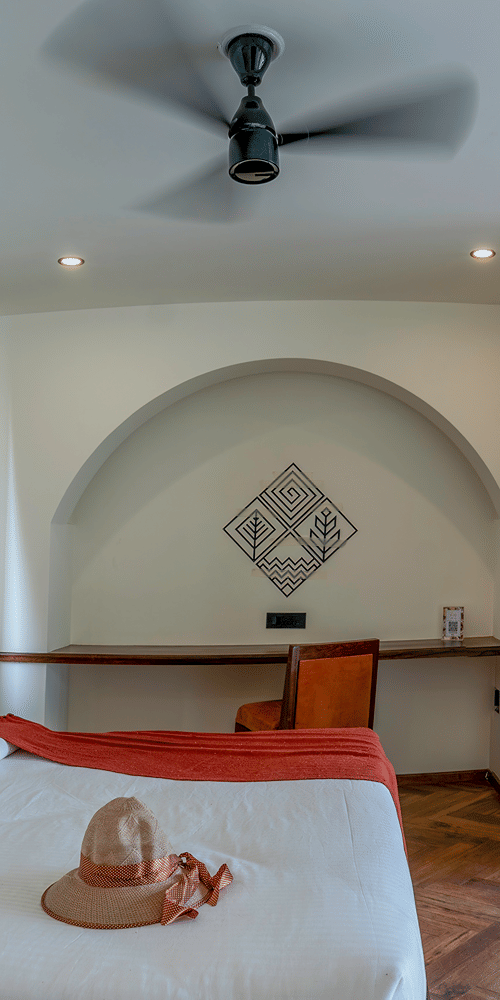 A bedroom with a large bed, an arched entryway leading to a sitting area with a sofa, and sliding glass doors opening to an outdoor area at The Golden Tusk, Jim Corbett