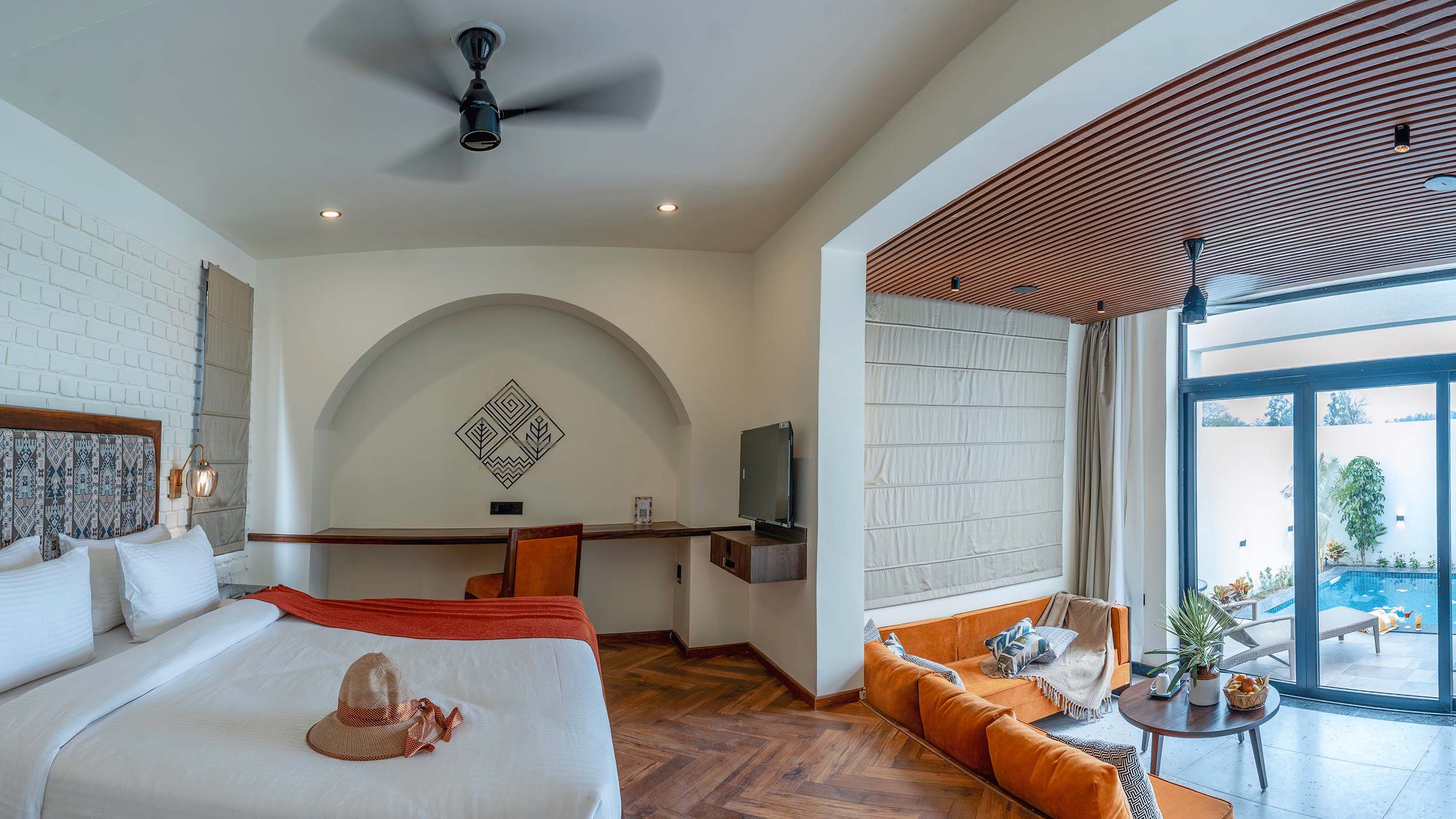 A bedroom with a large bed, an arched entryway leading to a sitting area with a sofa, and sliding glass doors opening to an outdoor area at The Golden Tusk, Jim Corbett