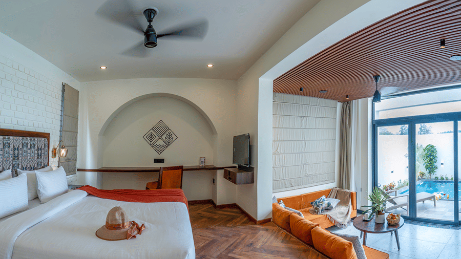 A bedroom with a large bed, an arched entryway leading to a sitting area with a sofa, and sliding glass doors opening to an outdoor area at The Golden Tusk, Jim Corbett