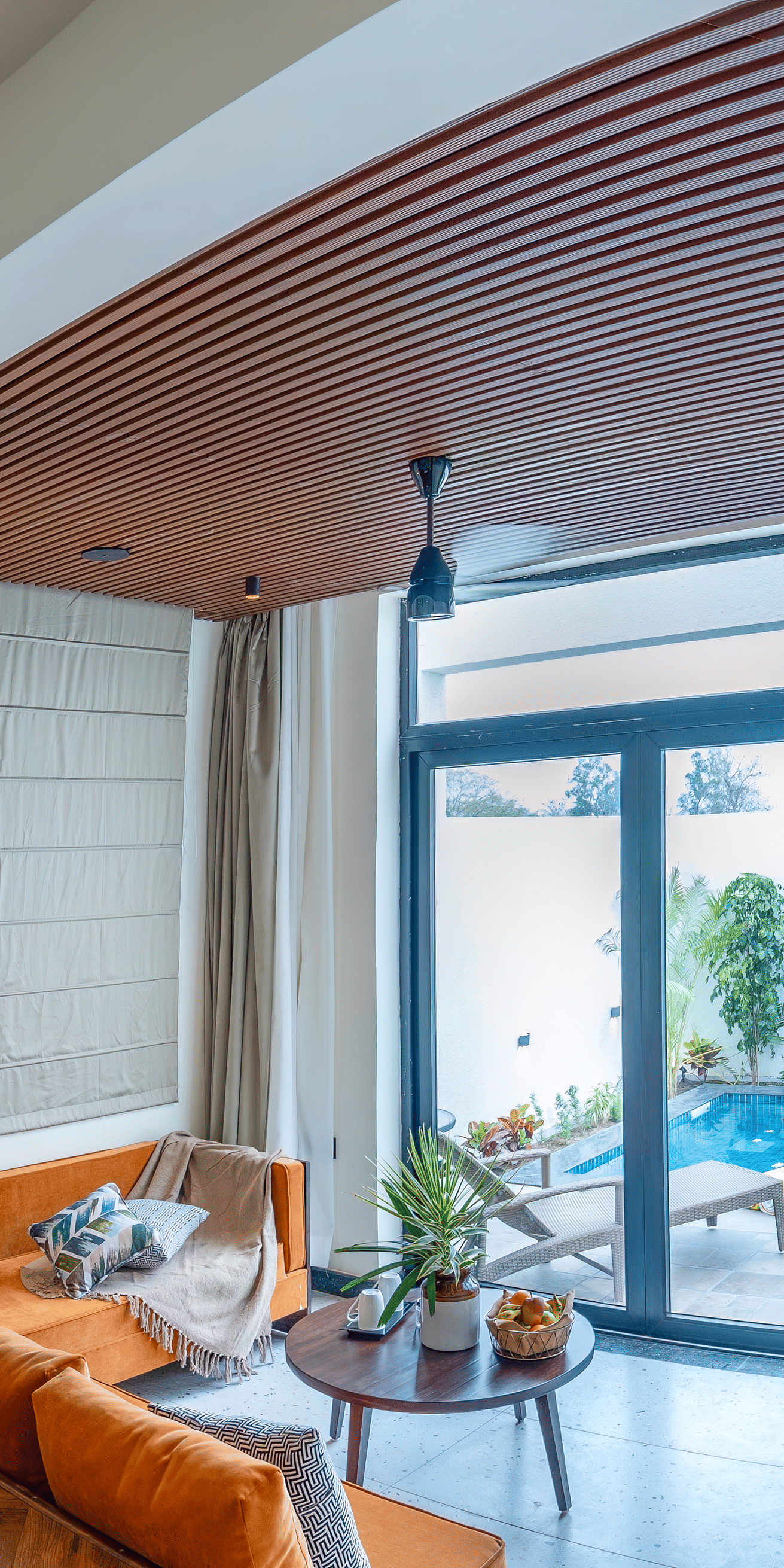 A bedroom with a large bed, an arched entryway leading to a sitting area with a sofa, and sliding glass doors opening to an outdoor area at The Golden Tusk, Jim Corbett