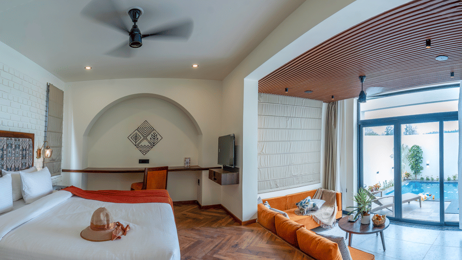 A bedroom with a large bed, an arched entryway leading to a sitting area with a sofa, and sliding glass doors opening to an outdoor area at The Golden Tusk, Jim Corbett