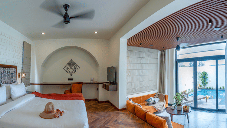 A bedroom with a large bed, an arched entryway leading to a sitting area with a sofa, and sliding glass doors opening to an outdoor area at The Golden Tusk, Jim Corbett