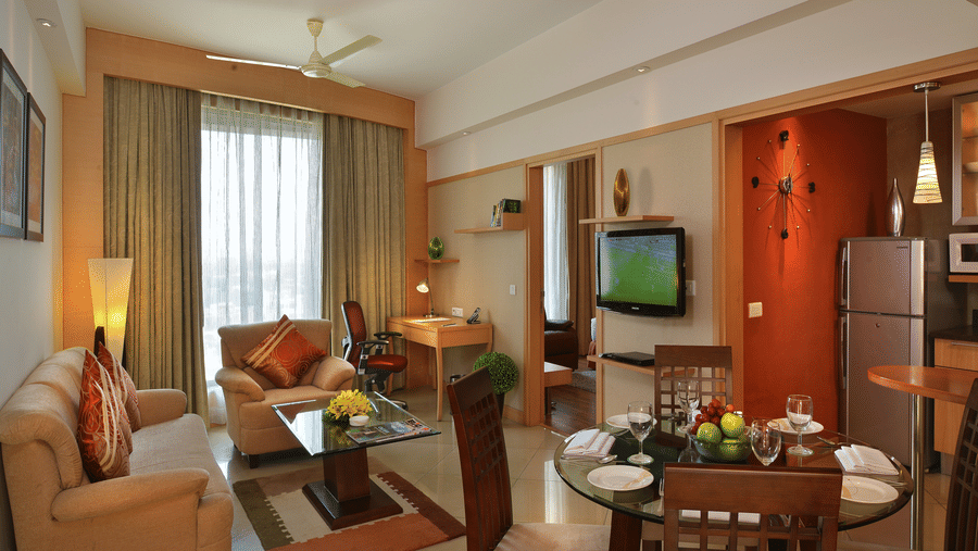 A premium suite at Savoy Suites, Manesar featuring a sating area with sofa set and centre table, flat TV screen, refrigerator, dining table, etc.