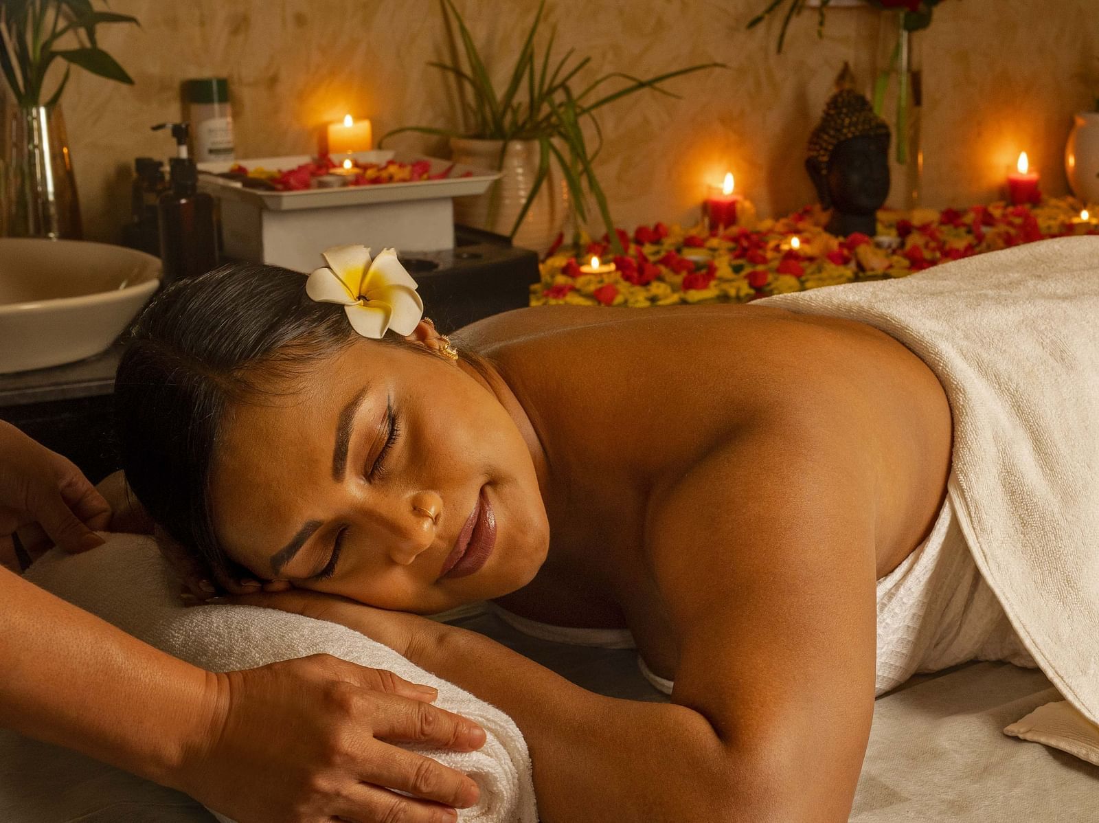 A close-up of a woman enjoying a relaxing massage in a serene spa setting. The warm lighting, candles, and flowers add to the tranquil ambiance - Coral Reef Resort & Spa, Havelock