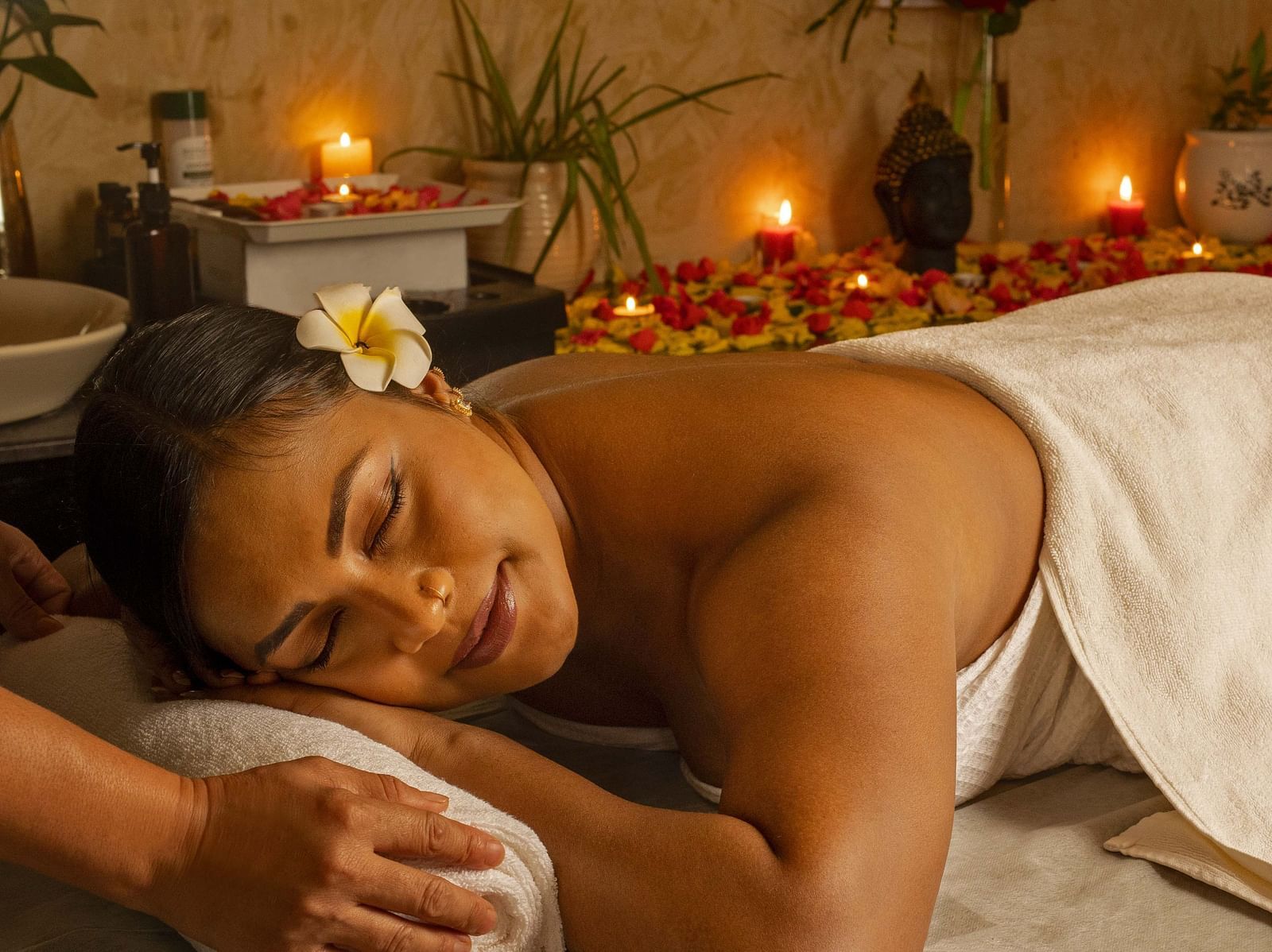 A close-up of a woman enjoying a relaxing massage in a serene spa setting. The warm lighting, candles, and flowers add to the tranquil ambiance - Coral Reef Resort & Spa, Havelock