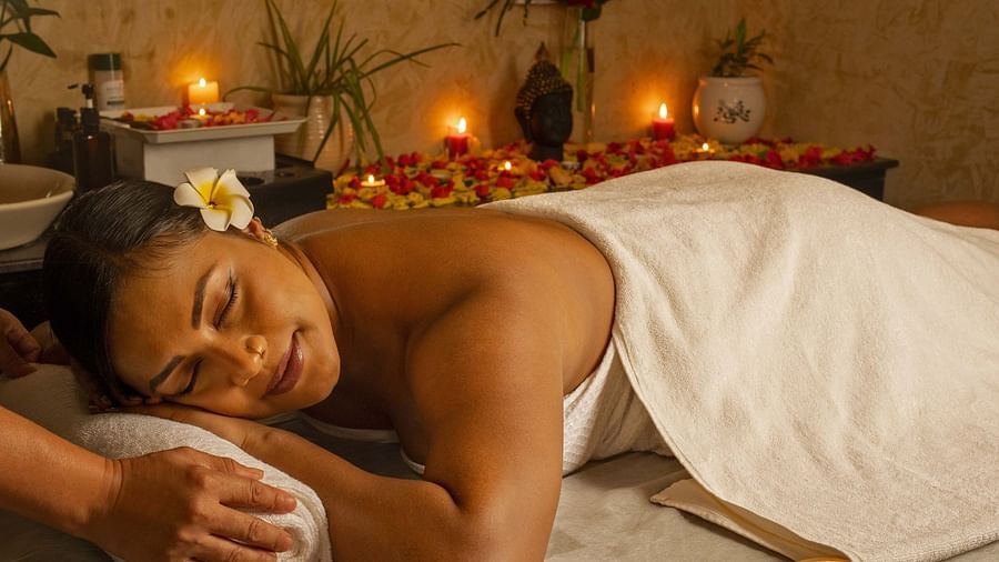 A close-up of a woman enjoying a relaxing massage in a serene spa setting. The warm lighting, candles, and flowers add to the tranquil ambiance - Coral Reef Resort & Spa, Havelock