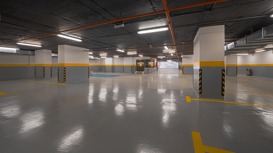 Parking space of Grand Iva Hotel, Abha, situated in the basement with ample overhead lighting, painted pillars, and flooring reflecting the lights.