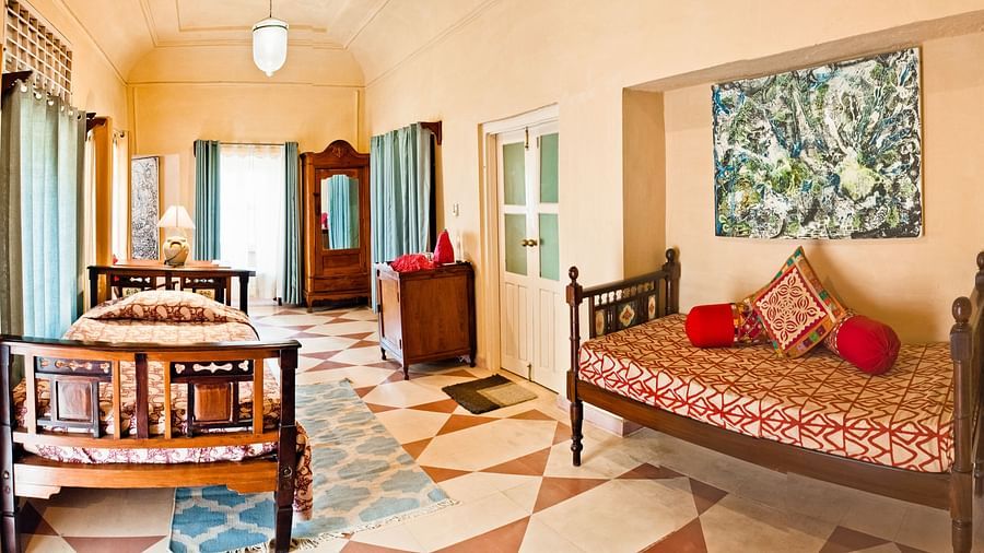 A bedroom with two beds, a wardrobe, and a painting in Tijara Fort-Palace - 19th Century, Alwar.