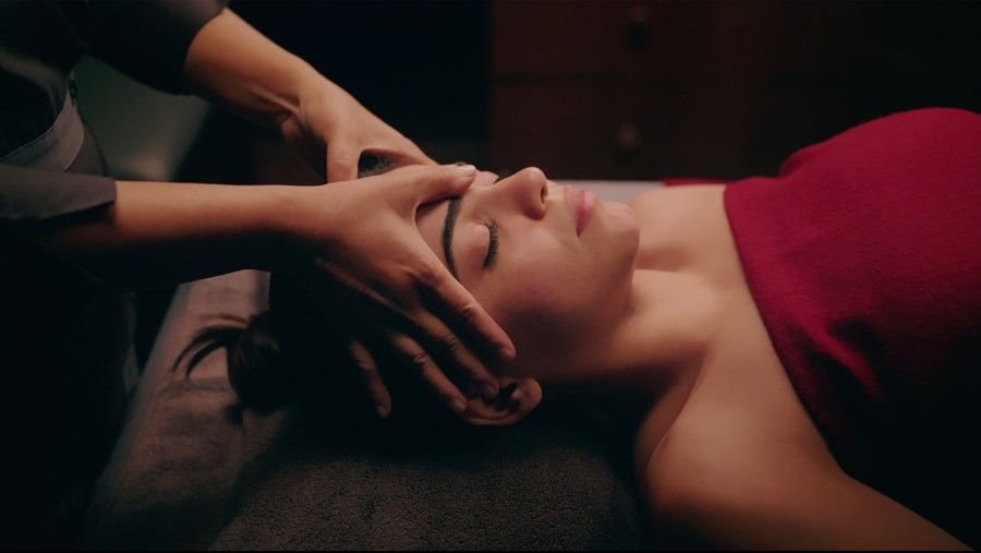 Woman lying on a spa bed with eyes closed, receiving a relaxing forehead and head massage while draped in a red towel - Marasa Sarovar Premiere, Bodhgaya