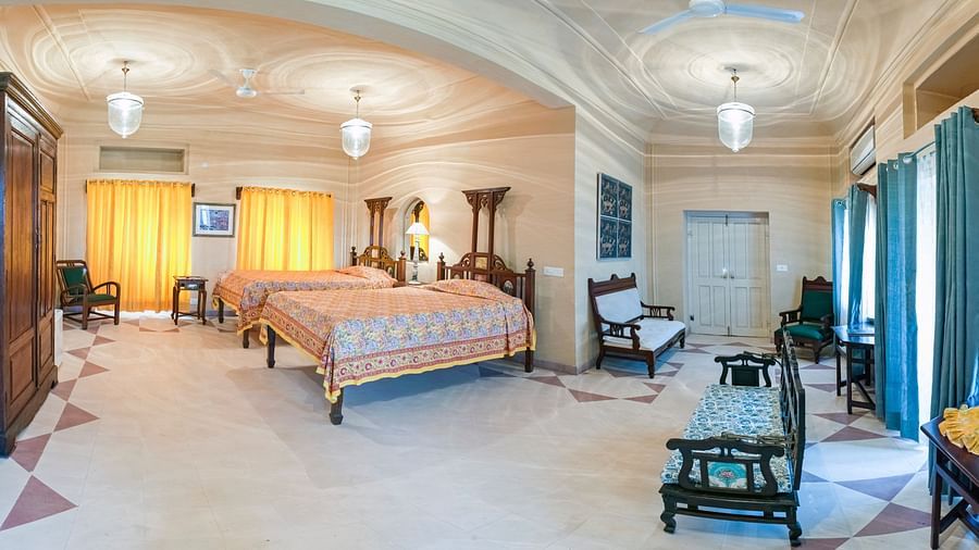 A wide shot of a bedroom with two beds, chairs, a wardrobe, and windows in Tijara Fort-Palace - 19th Century, Alwar.