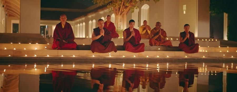 Monks in red robes meditating on candlelit steps at night, their reflections glowing in a calm water pool, creating a serene and spiritual atmosphere - Marasa Sarovar Premiere, Bodhgaya