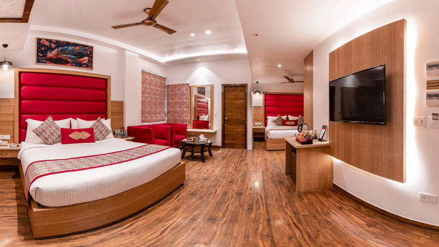 Side view of a Family Room at Lords Inn Amritsar with a king bed, red headboard, wall-mounted TV, wooden flooring, and warm ambient lighting.