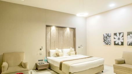 Another view of a well-lit hotel room with a king size bed and a comfortable armchair | The Citi Residenci Hotel Durgapur