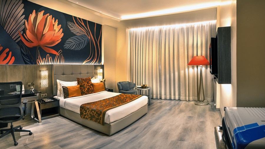 Superior room at The Sonnet, Kolkata featuring a king-size bed, stylish interiors, a work desk, lounge chair, floor-to-ceiling curtains, and warm ambient lighting.