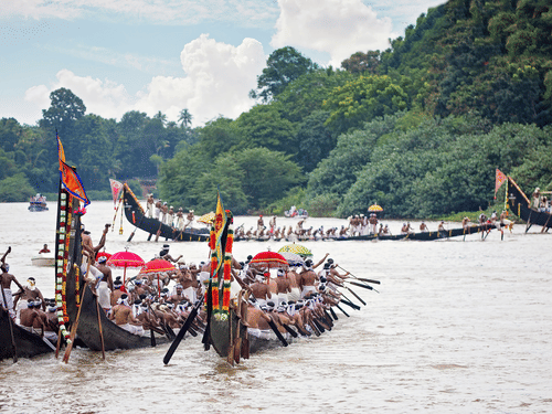 Snake boats filled with rowers race along the backwaters, a part of Onam Celebration in Kochi, during a traditional regatta, surrounded by lush green riverbanks and spectators