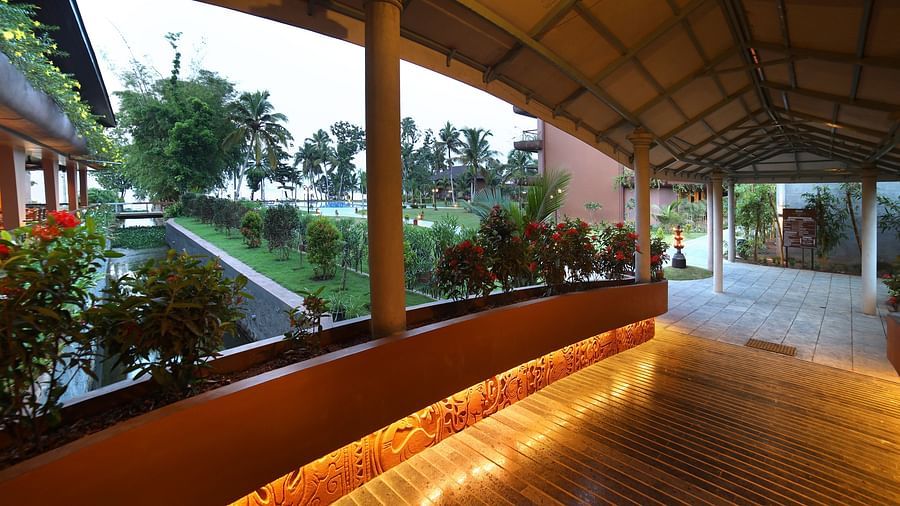 A covered walkway at Uday Backwater Resort, illuminated with warm lighting, surrounded by lush greenery, and overlooking a tranquil garden in the evening
