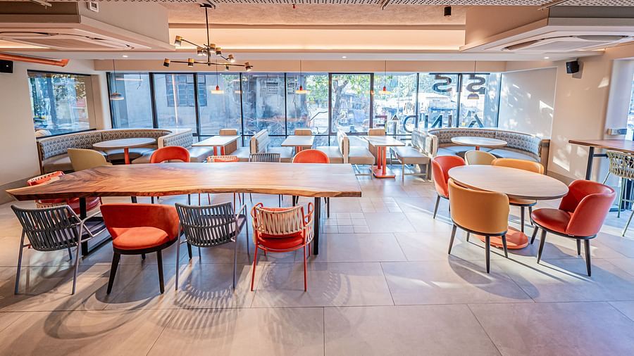 A large rectangular table with chairs on both sides and a round table with chairs around it, with glass panels in the background, at Indie Stays Mumbai International Airport.