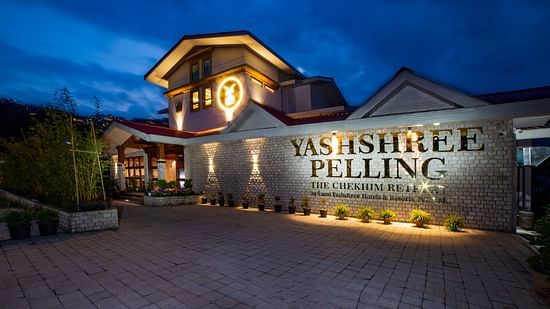 Elegant nighttime view of Yashshree Pelling, a luxury resort with warm lighting, modern stone facade, and scenic mountain surroundings.