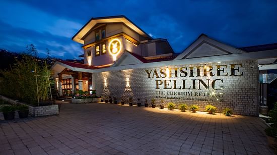Elegant nighttime view of Yashshree Pelling, a luxury resort with warm lighting, modern stone facade, and scenic mountain surroundings.