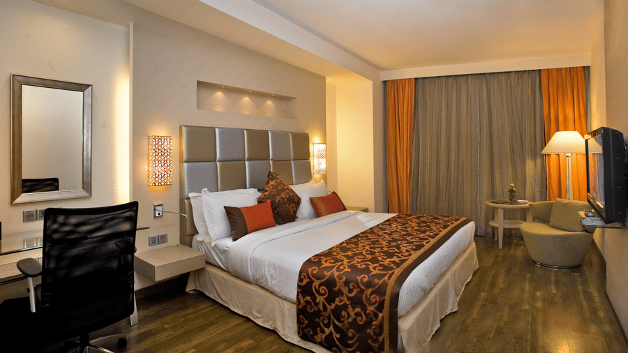 Interior of a hotel room showcasing its furnishings and amenities, including a bed, a desk, a TV and a chair- The Sonnet, Kolkata.