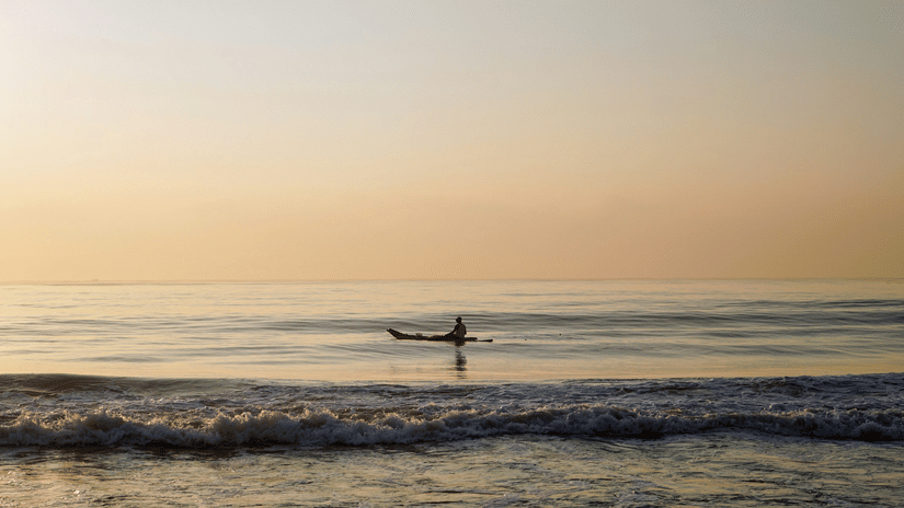 A person travelling on a boat in Elliots Beach in Chennai after the sun set, with waves overlapping the shoreline.