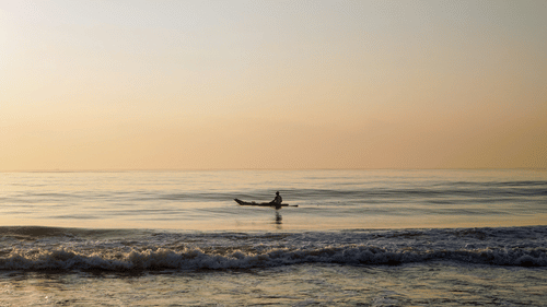 A person travelling on a boat in Elliots Beach in Chennai after the sun set, with waves overlapping the shoreline.