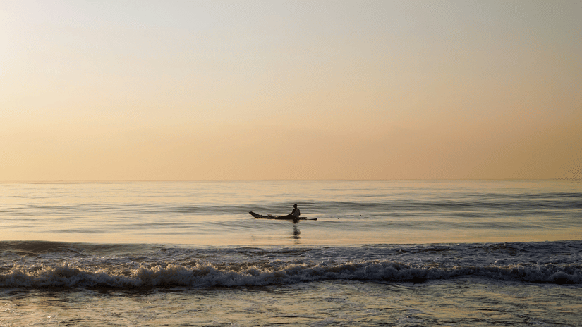 A person travelling on a boat in Elliots Beach in Chennai after the sun set, with waves overlapping the shoreline.
