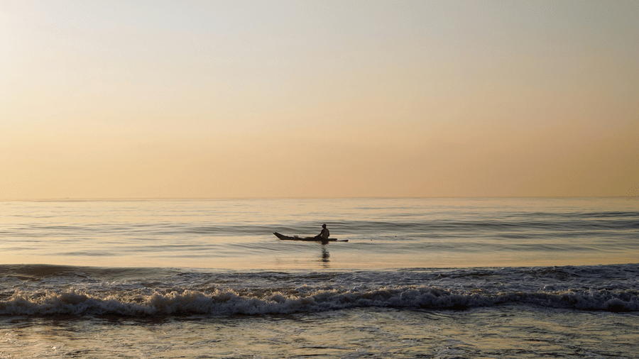 A person travelling on a boat in Elliots Beach in Chennai after the sun set, with waves overlapping the shoreline.