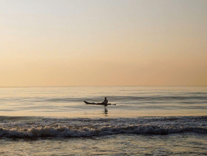 A person travelling on a boat in Elliots Beach in Chennai after the sun set, with waves overlapping the shoreline.