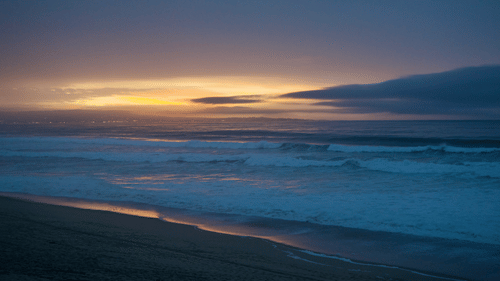 A beautiful sunset over the ocean with waves crashing on the shore.