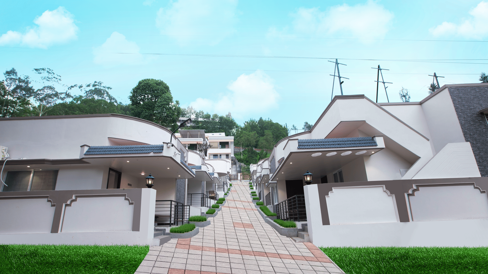 A wide-angle shot of the exterior of WOW Naturfull Resorts, Yercaud, with a bright blue sky in the background and a bricked pathway in the middle going upwards.
